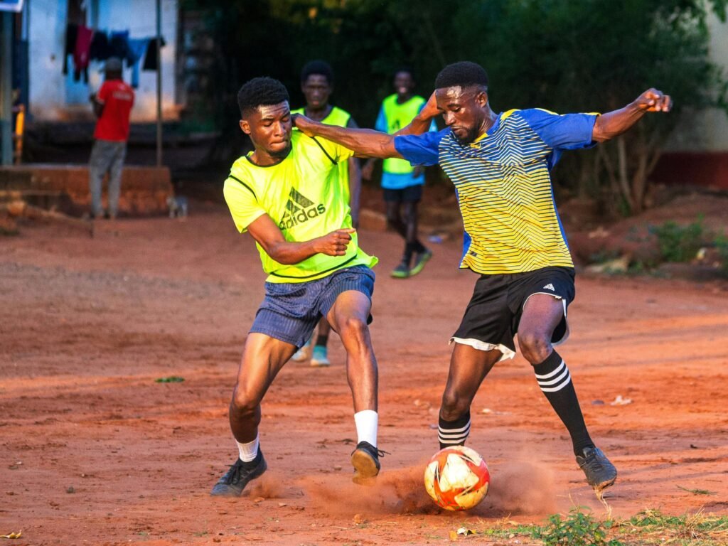 Dynamic soccer game in Accra showing young athletes playing on a dirt field.