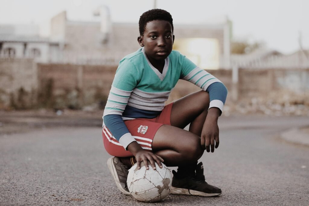 Casual portrait of a young boy in streetwear posing with a soccer ball outdoors.