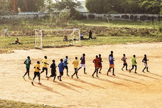 A group of young men practicing soccer on a dirt field under the sun.